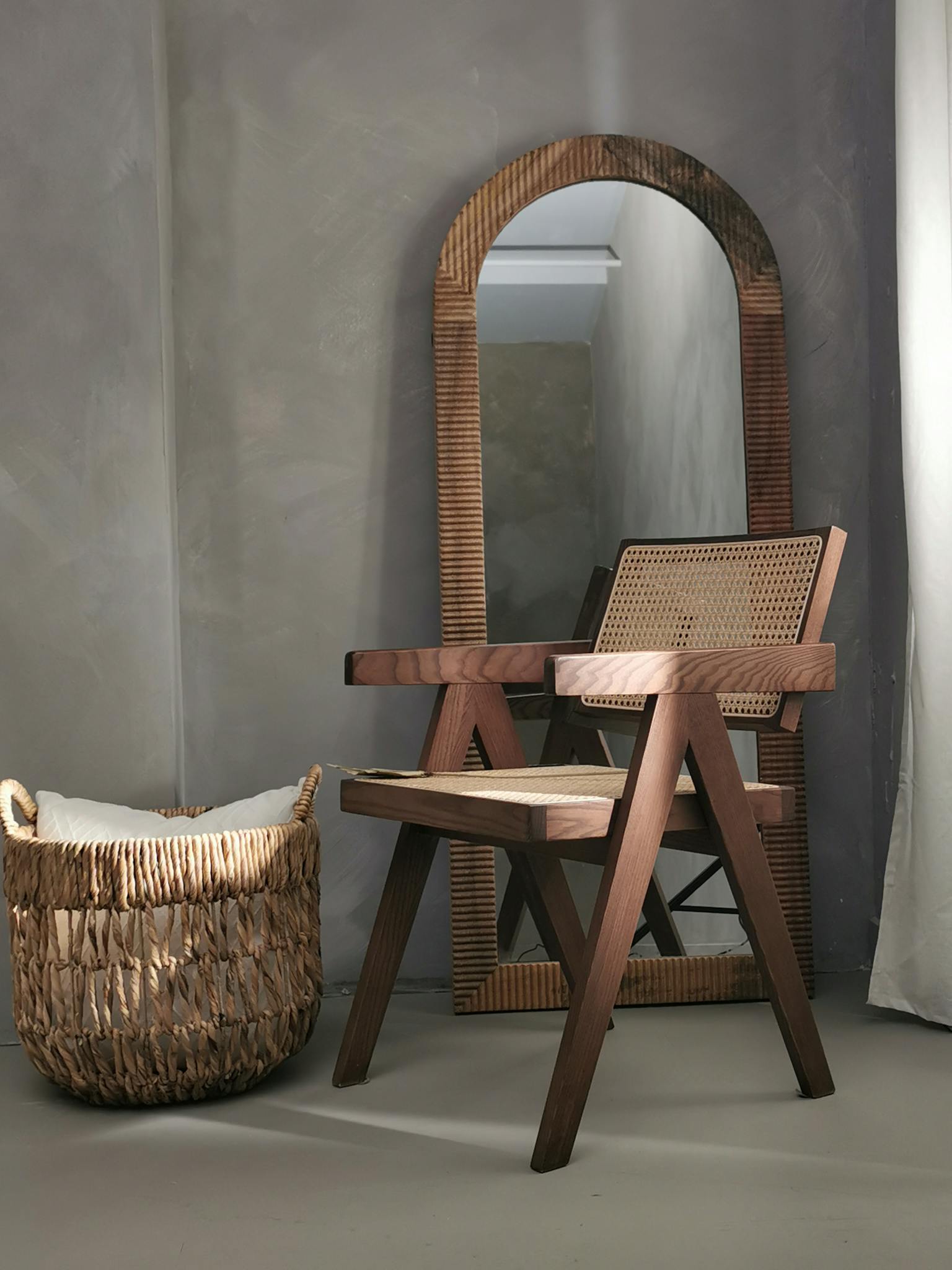 Cozy bohemian corner with a wooden armchair, round mirror, and rattan basket.
